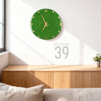 A green wall clock with gold-colored hands and Roman numerals. The clock is round and mounted on a white wall. The text "ART STUDIO 39" is in a circle below the clock.