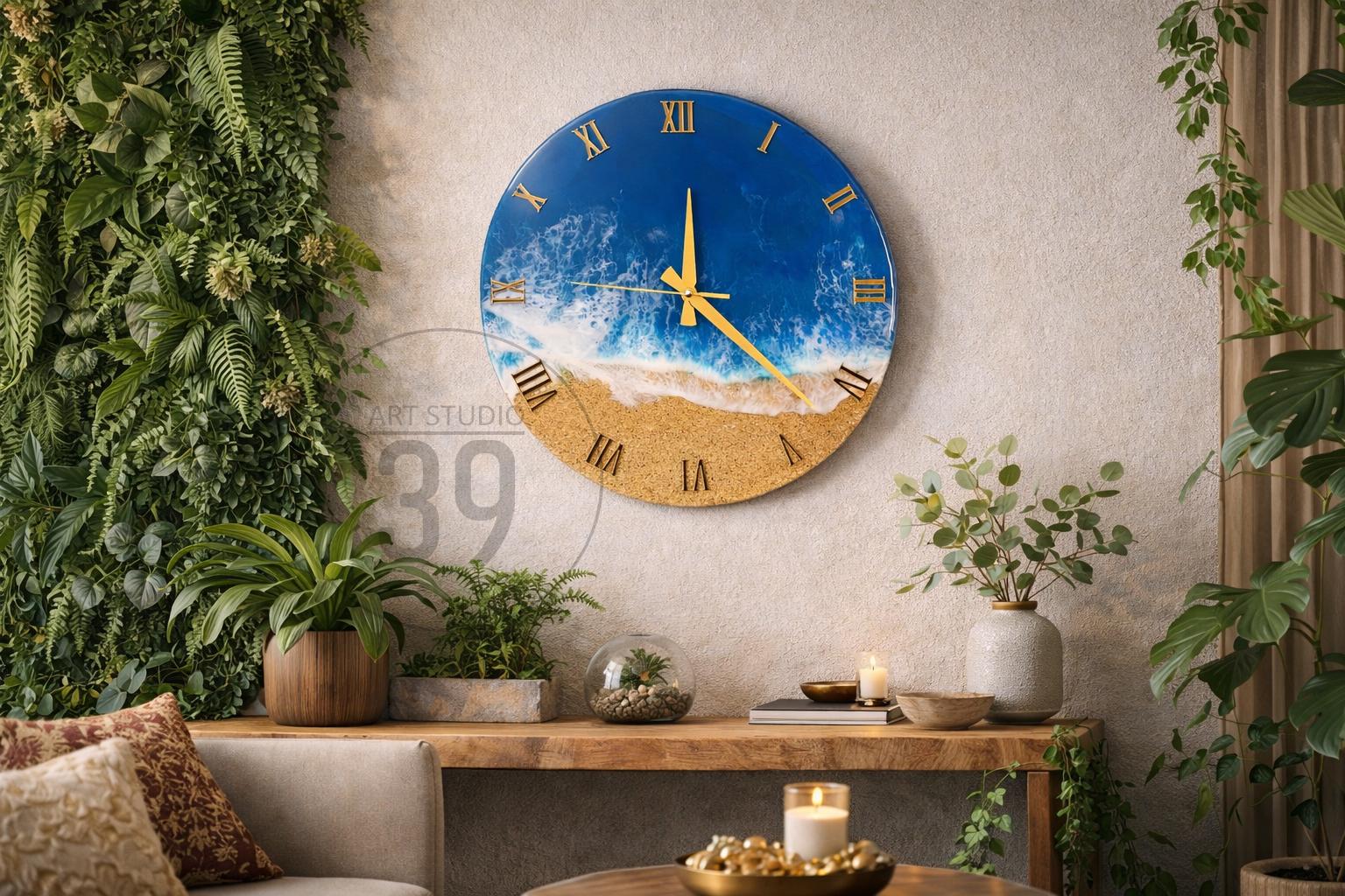 A round wall clock with a beach scene design. The top half features a blue ocean with white waves, while the bottom half depicts a sandy beach. Gold Roman numerals mark the hours. The clock hands are gold.