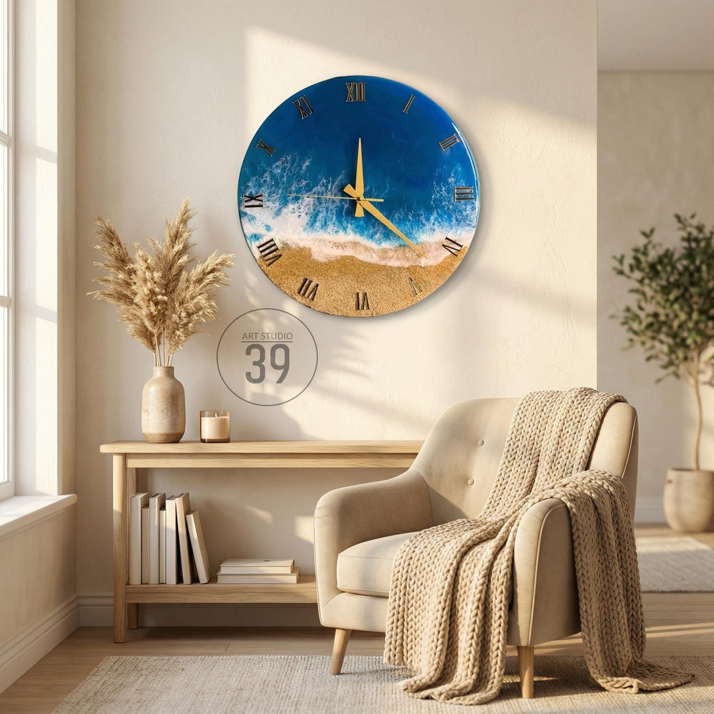 A round wall clock with a beach scene design. The clock face features a blue ocean, white waves, and a sandy beach. Gold-colored hands and Roman numerals mark the time. The clock is mounted on a beige wall.