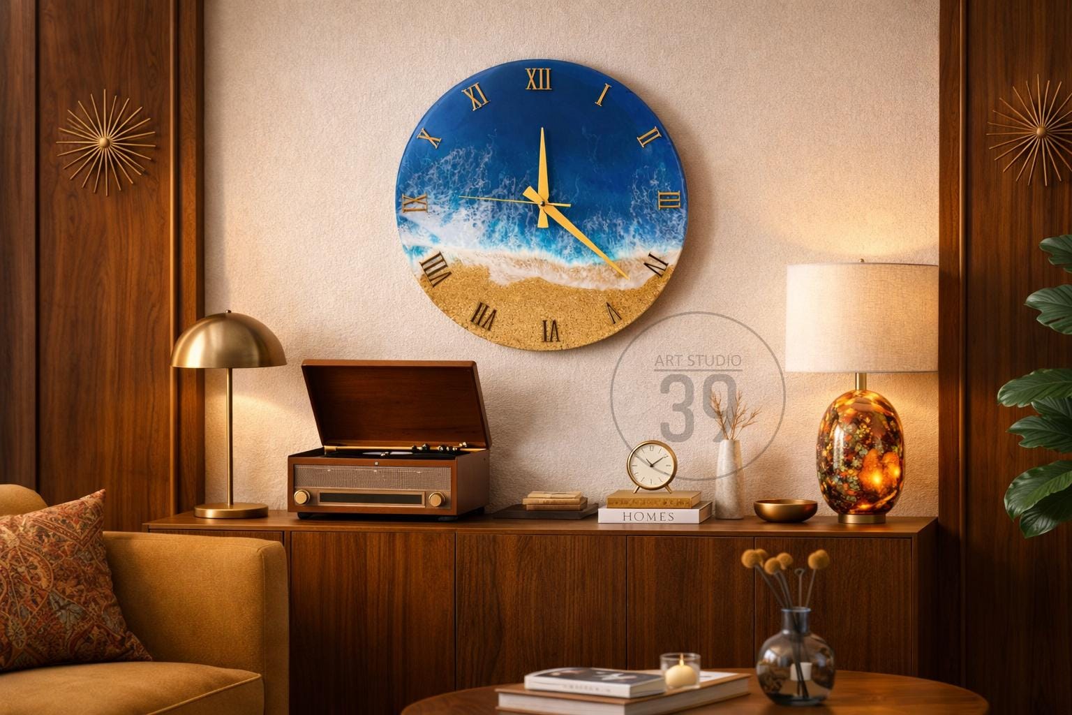 A round wall clock with a beach scene design. The clock face features a blue ocean, white waves, and a sandy beach. Gold Roman numerals and clock hands complete the design. The clock is mounted on a beige wall.