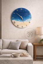A round wall clock with a blue and white ocean-themed design. The clock face features Roman numerals and silver hands. The clock is mounted on a light-colored wall above a sofa and coffee table.
