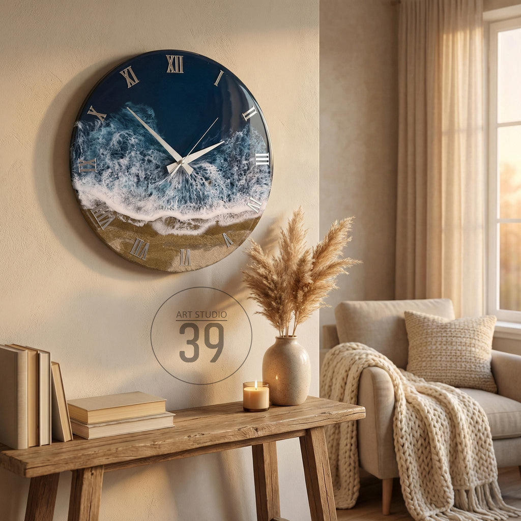 A round wall clock with a coastal design. The clock face features a dark blue ocean scene with white waves and a sandy beach. Silver Roman numerals mark the hours. The clock is mounted on a beige wall.