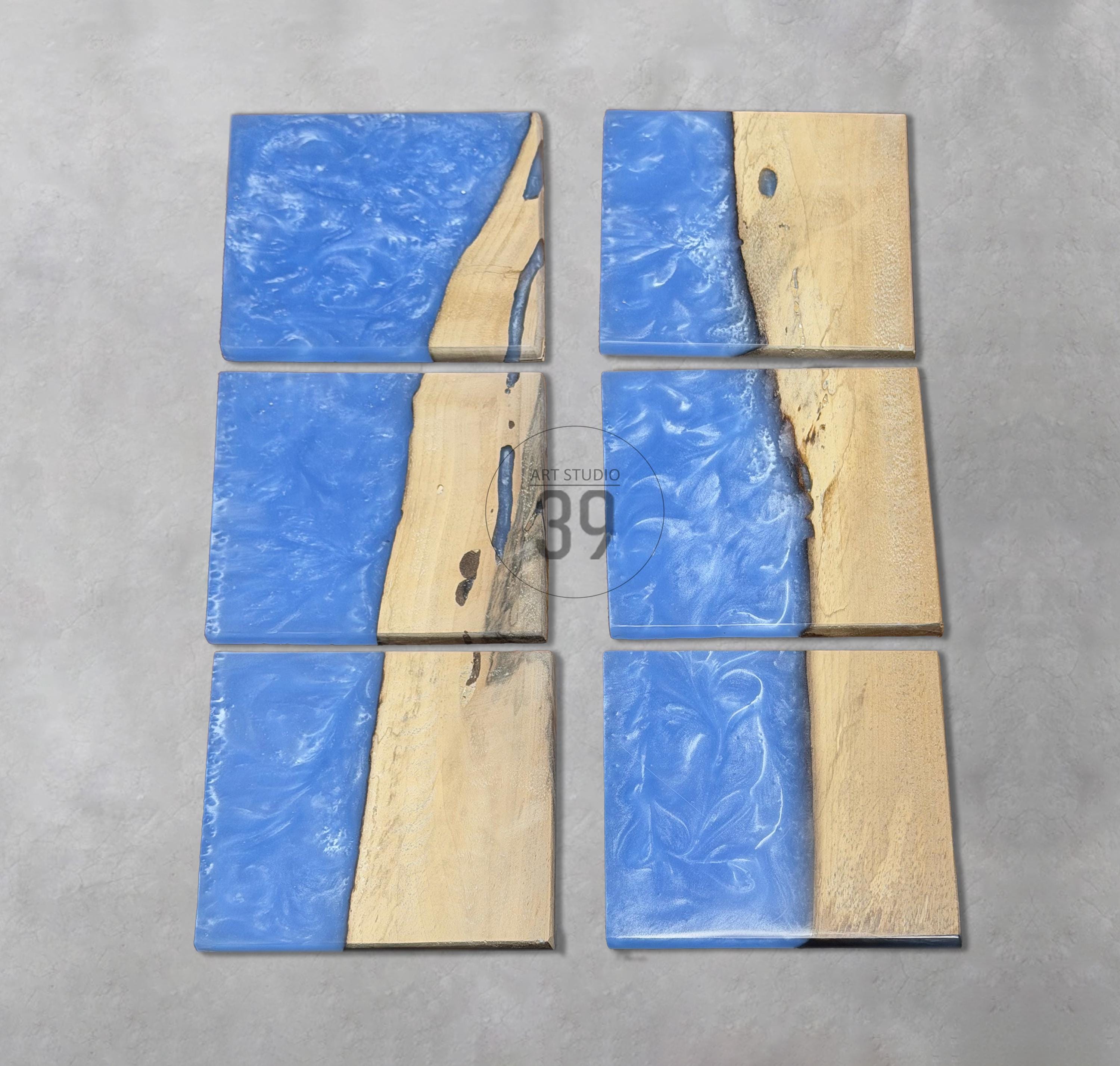 Six square coasters with a unique design. Each coaster features a combination of light blue resin and natural wood. The resin has a textured appearance, and the wood has a light brown color. The coasters are arranged on a gray surface.