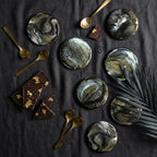 An overhead shot features several round coasters with a black, white, and gold marbled design. Gold spoons and pieces of chocolate with gold leaf accents are scattered around the coasters. The number 39 is visible.