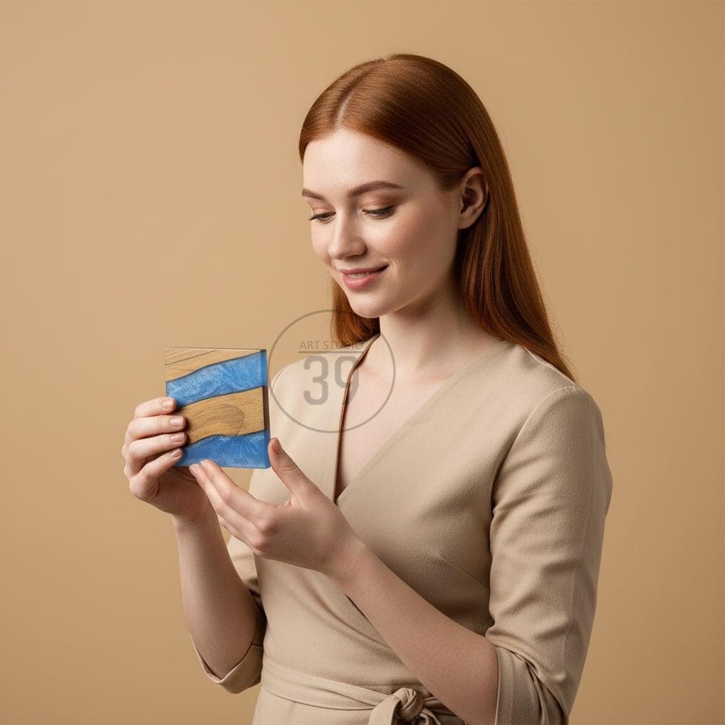 A square wooden coaster with a blue and brown resin design. The coaster is held by a person with red hair, and the background is a solid tan color. The coaster has a unique, artistic appearance.