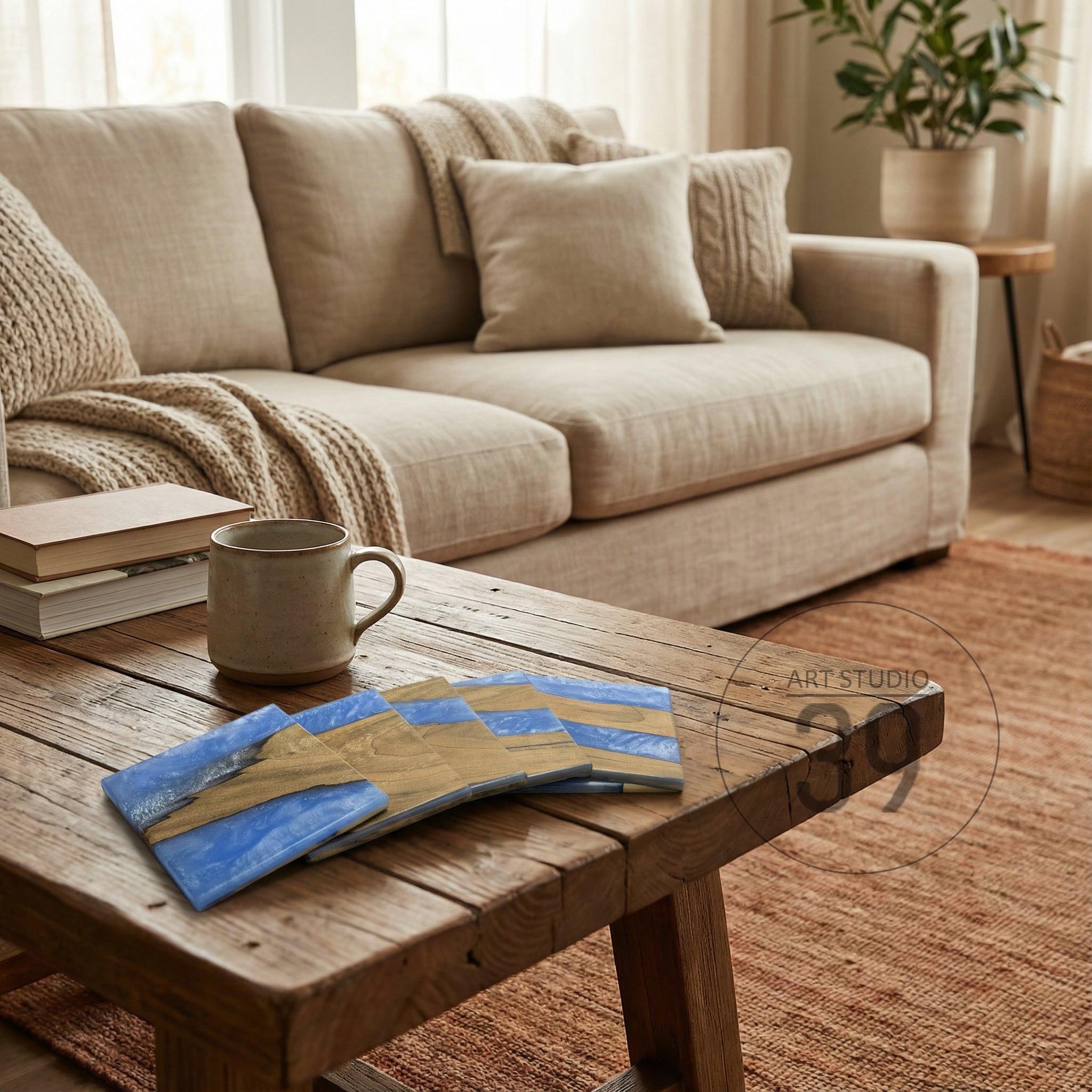 A set of four square coasters with a wood and blue resin design. The coasters are stacked on a rustic wooden coffee table, with a beige sofa and rug in the background.