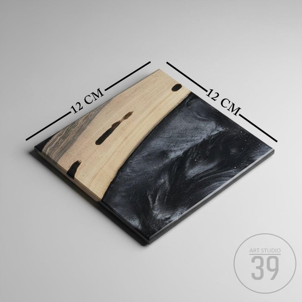 Square wooden serving board, 12 cm x 12 cm, with a light wood grain finish on one side and a black resin design on the other. The board has a dark border and is from Art Studio 39.