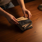 A stack of wooden coasters with a two-tone design. The top half of each coaster is light-colored wood, while the bottom half features a dark, swirled resin. The coasters are being handled.