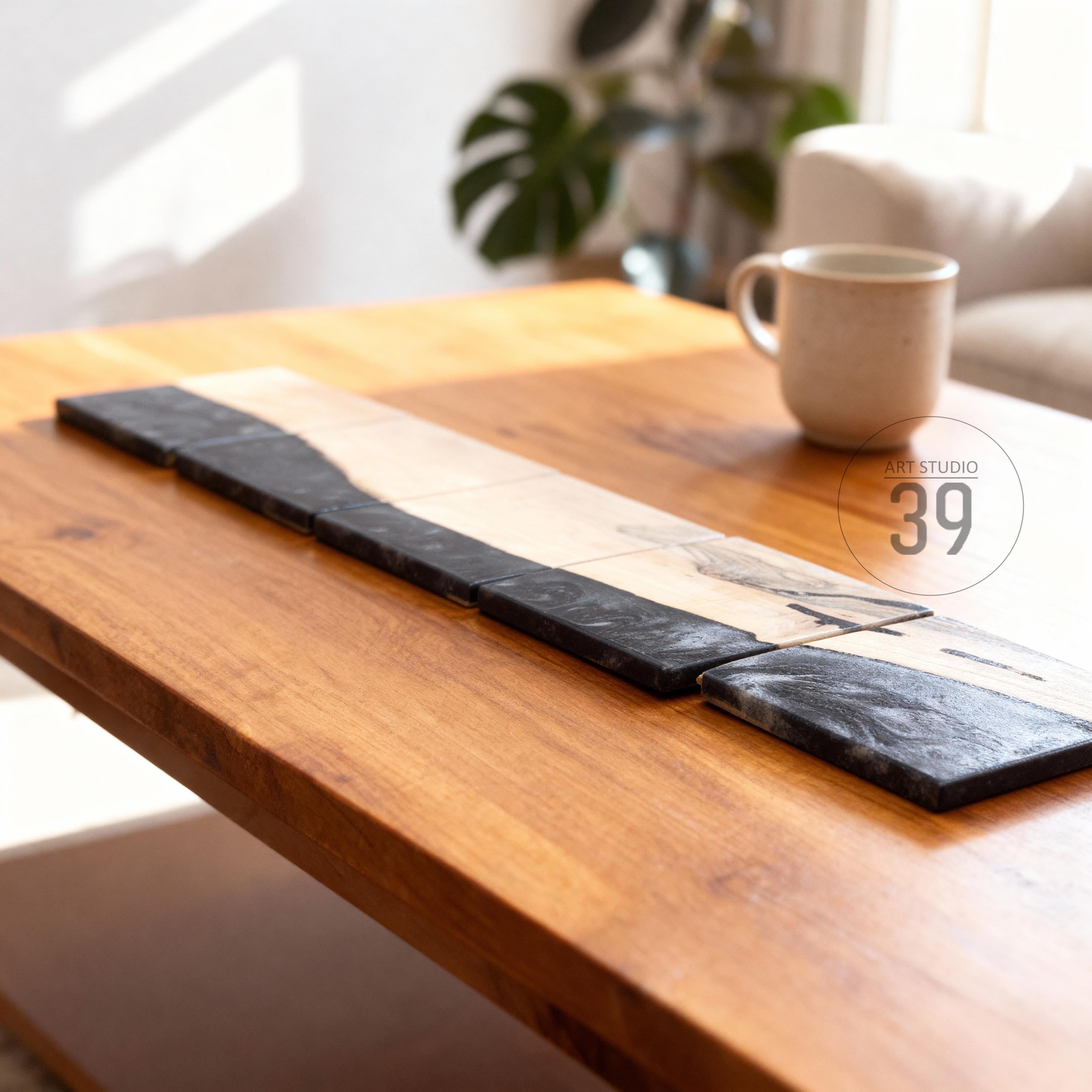 A wooden coffee table with a rectangular design. A long, decorative piece with black and light wood sections is placed on the table. A beige mug sits on the table. The text "ART STUDIO 39" is visible.