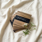 A stack of square wooden coasters with a dark, black resin inlay. The coasters have a natural wood grain pattern and the text "39" is visible. A sprig of white flowers rests beside the coasters.