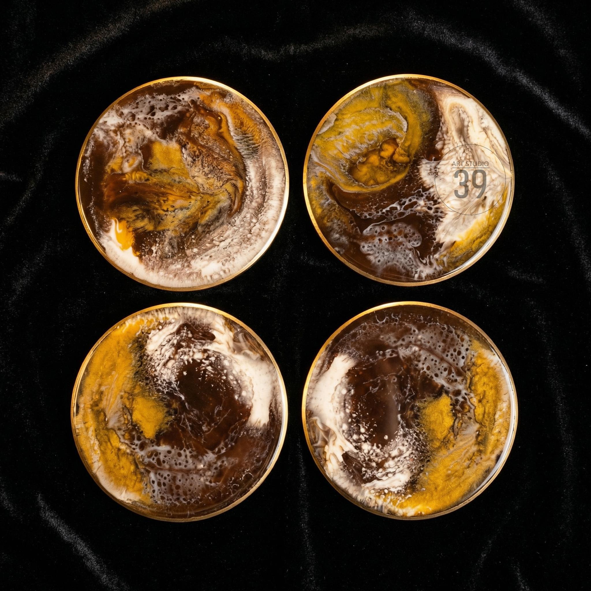 Set of four round coasters with a gold rim. The coasters feature a swirling design in shades of brown, yellow, and white. One coaster has the number "39" printed on it. The coasters are displayed on a black surface.