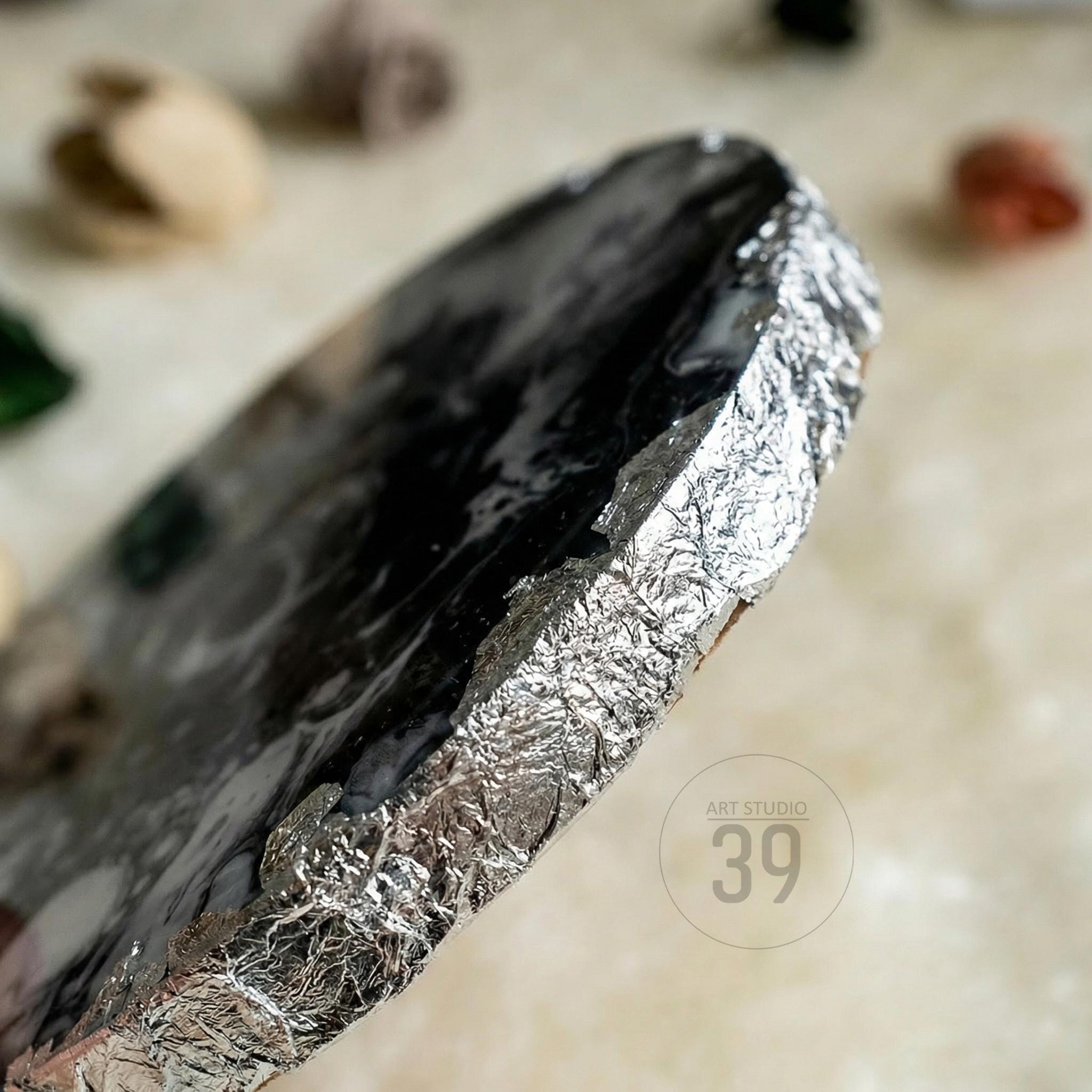 Close-up of a handmade, oval-shaped art piece with a dark, glossy surface. The edges are wrapped in silver foil, creating a textured border. The text "ART STUDIO 39" is visible in the lower right corner.