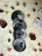 Four round coasters with a black and white marbled design are stacked on a white, textured surface. The coasters are surrounded by dried flowers and leaves. The bottom right coaster has the text "ART STUDIO 39".