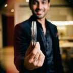 A person holding two silver-colored, circular objects. The objects have a textured edge and appear to be made of metal. The number "39" is printed on the person's hand. The person is wearing a black suit.