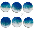 Six round coasters with a resin ocean wave design. The coasters feature shades of blue, teal, and white, with a glossy finish. The text "ART STUDIO 39" is in the center.
