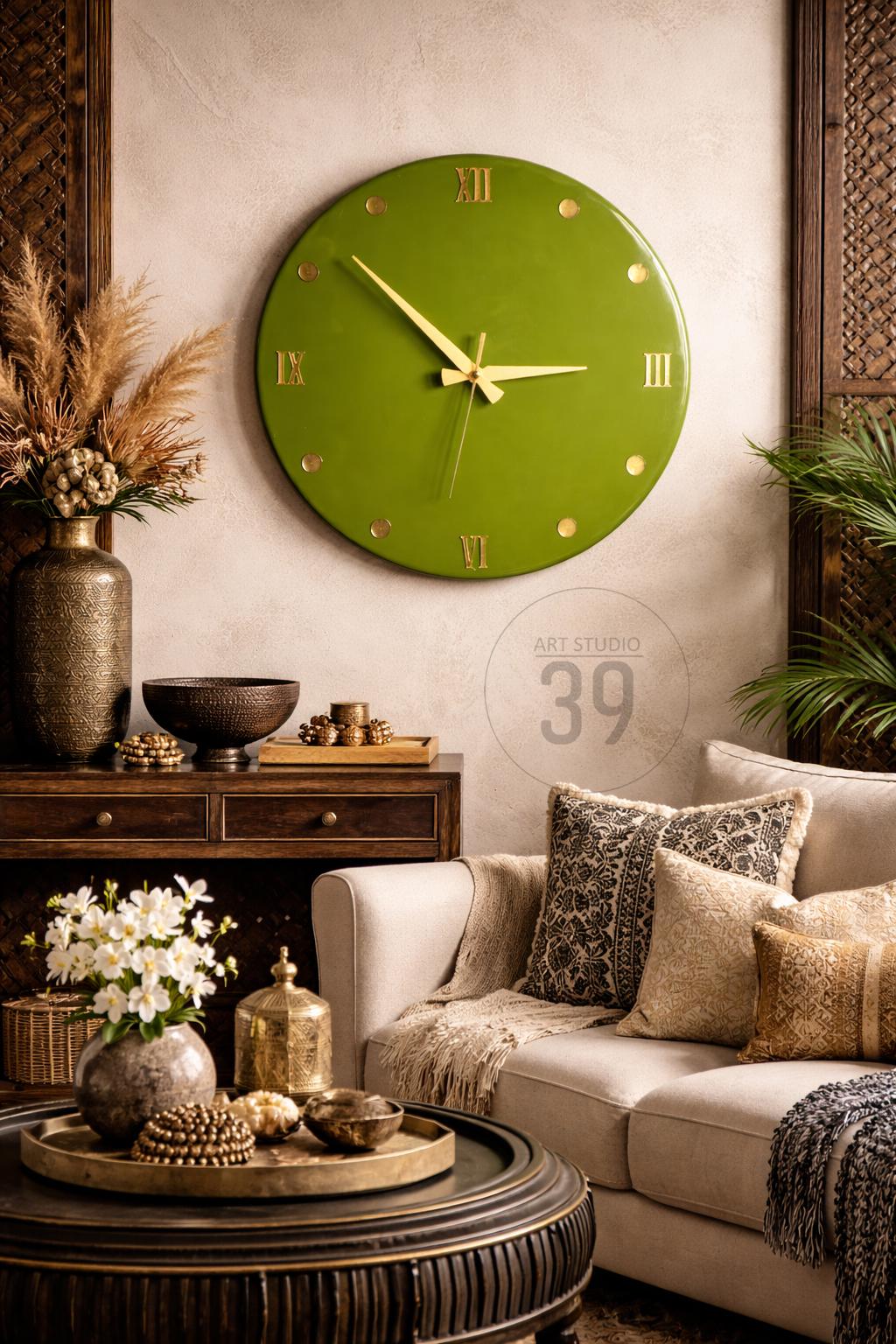 A large, round, olive green wall clock with gold-colored hands and Roman numerals. The clock is mounted on a neutral-colored wall, with decorative elements like a sofa, pillows, and a coffee table.