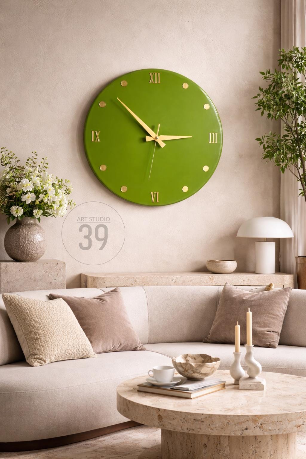 A large, round, green wall clock with gold-colored hands and hour markers. The clock is mounted on a neutral-colored wall above a cream-colored sofa with decorative pillows. The image includes the text "ART STUDIO 39".