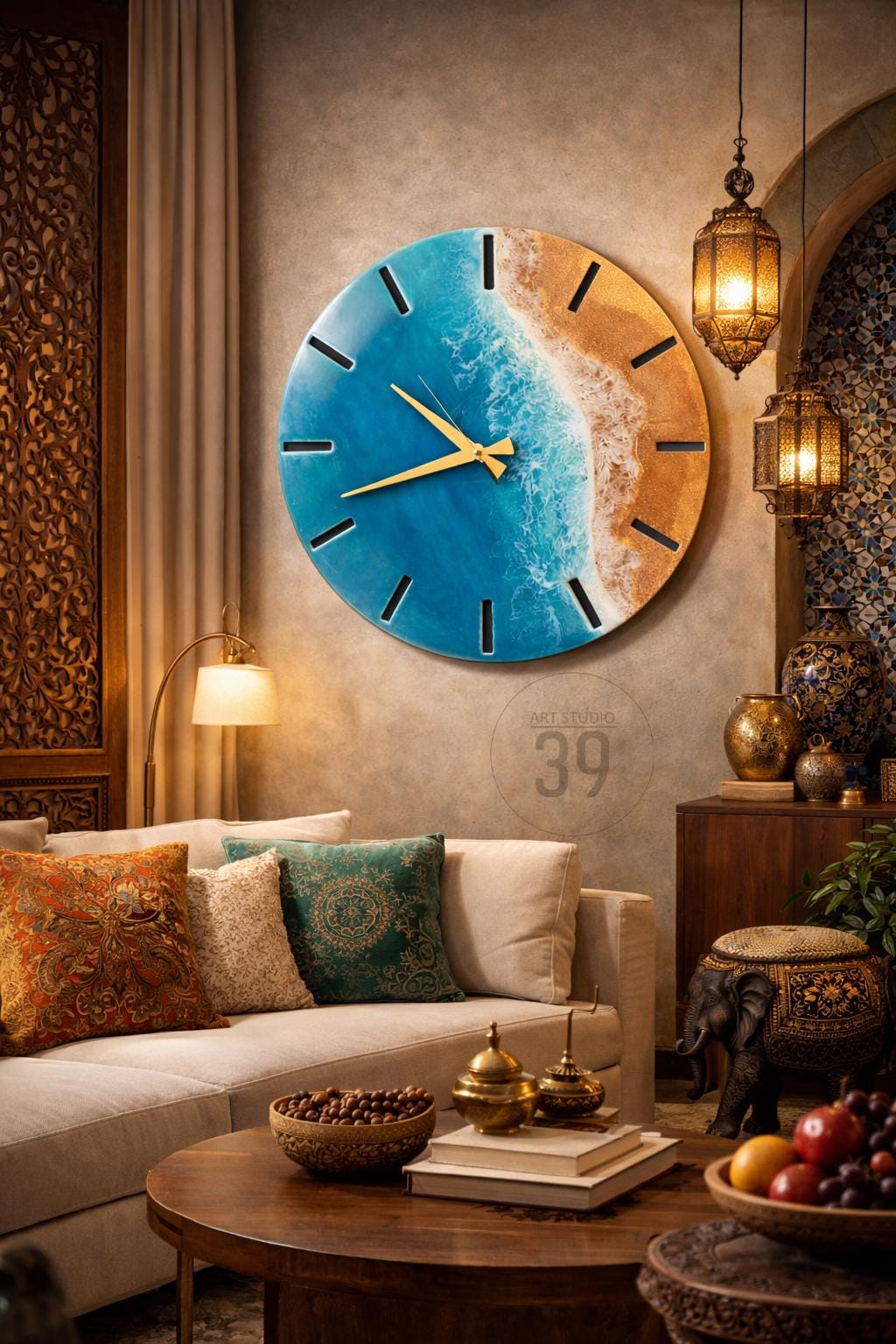 A large, round wall clock with a beach-themed design. The clock face features a blue ocean and sandy beach, with gold-colored hands and hour markers. The text "ART STUDIO 39" is visible. The clock is mounted on a neutral-colored wall.