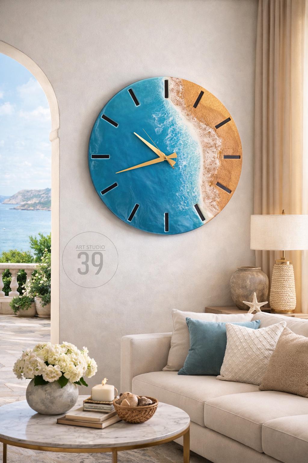 Round wall clock with a beach-themed design. The clock face features a blue ocean and sandy beach, with gold-colored hands and black hour markers. The clock is hanging on a light-colored wall. The text "ART STUDIO 39" is visible.