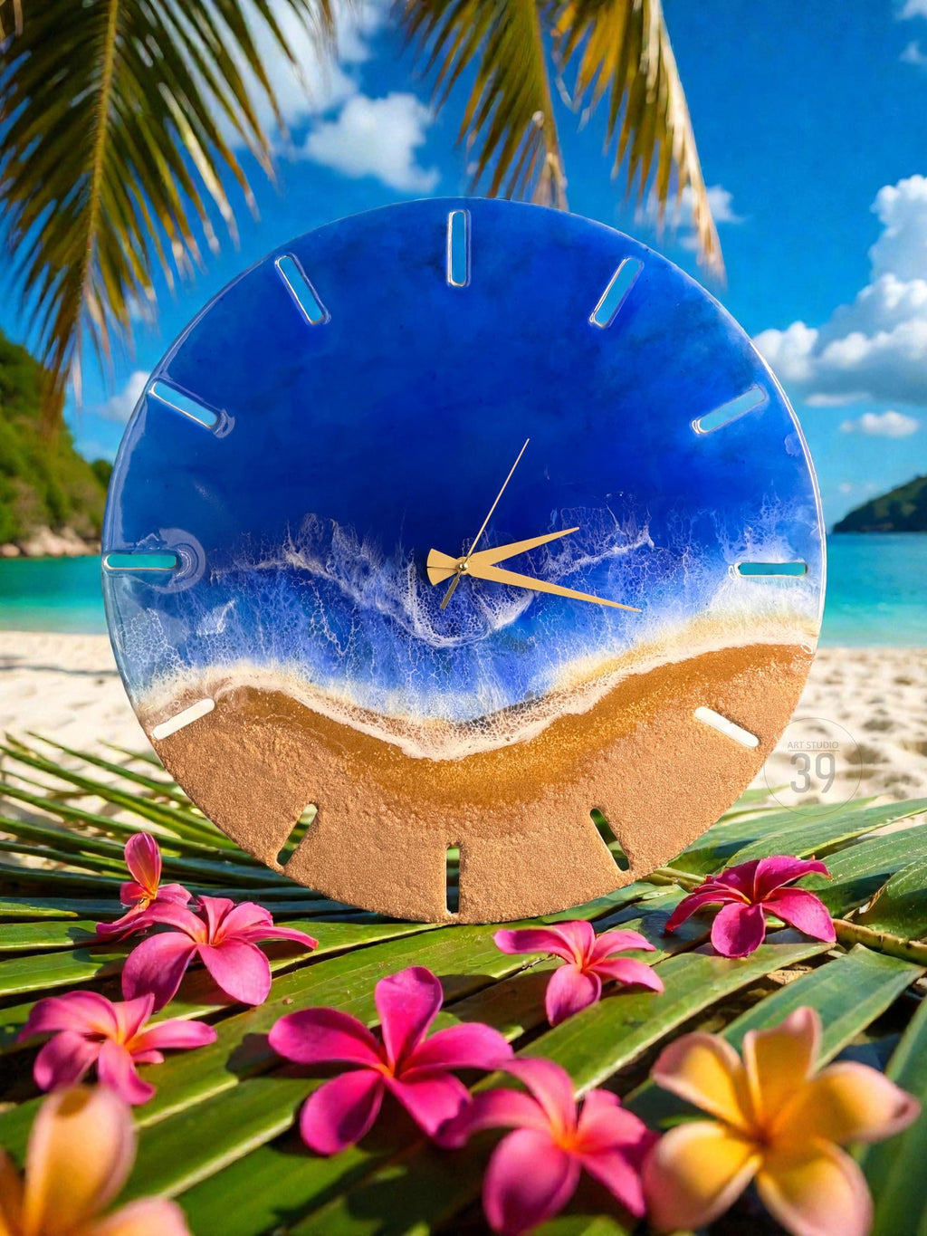 A round wall clock with a beach-themed design. The clock face features a blue resin ocean, a golden sand-colored bottom, and gold-colored clock hands. Pink and yellow flowers and green leaves are in the foreground.