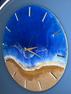 Round wall clock with a beach-themed design. The clock face features a blue ocean and golden sand, with white foamy waves. The clock has gold hands and white markers. The number "39" is visible on the clock face.