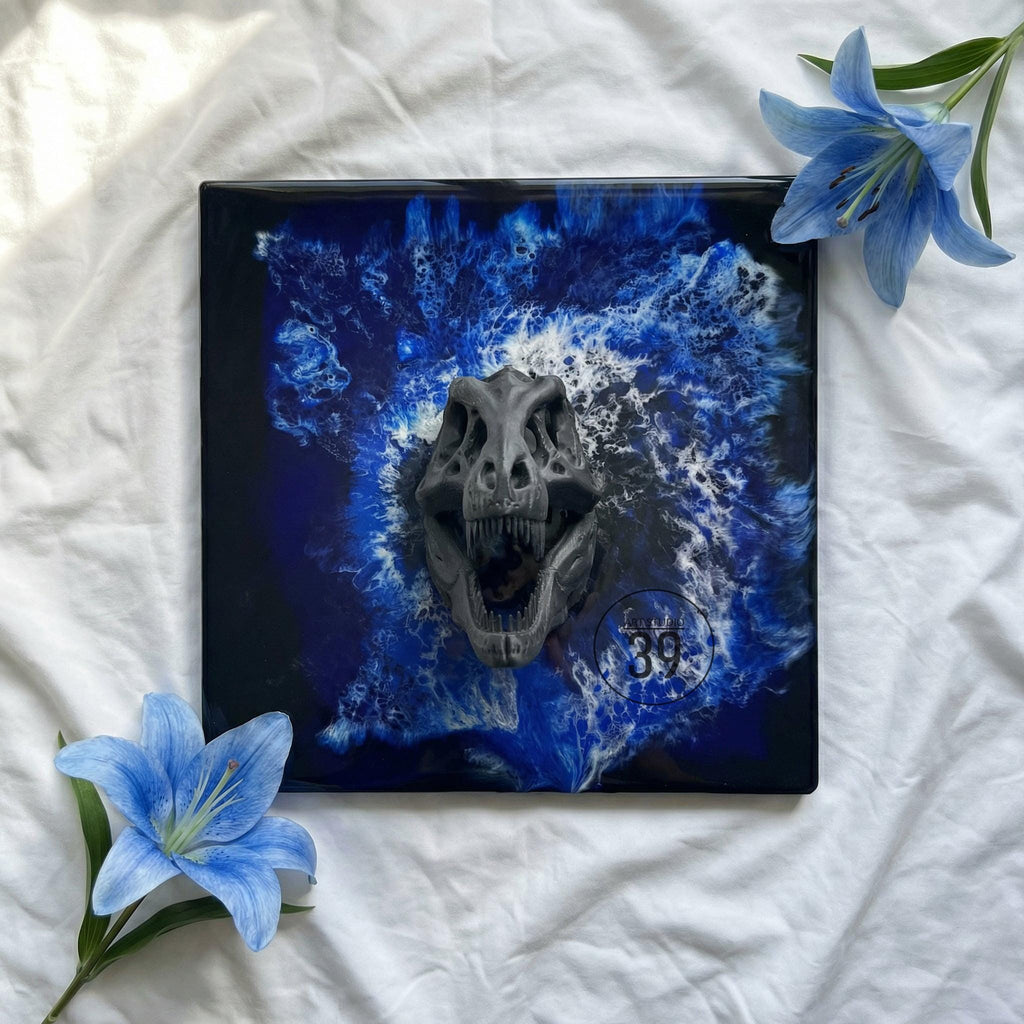Square artwork featuring a gray dinosaur skull against a blue and white abstract background. The artwork has a glossy finish and includes the number 39 in a circle. Blue flowers are placed around the artwork.