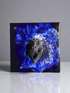 A square, dark artwork featuring a detailed, dark gray dinosaur skull emerging from a vibrant blue and white abstract design. The number "39" is visible in the lower right corner. The artwork has a glossy finish.