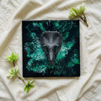 A square, black decorative piece featuring a gray triceratops skull. The background has a swirling green and black design. The number "39" is visible in the lower left corner. Green flowers are placed around the piece.