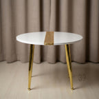 A round white side table with gold-colored legs and a gold stripe down the center of the tabletop. The table has a modern design and is suitable for a living room or bedroom. The table is approximately 20 inches in diameter.