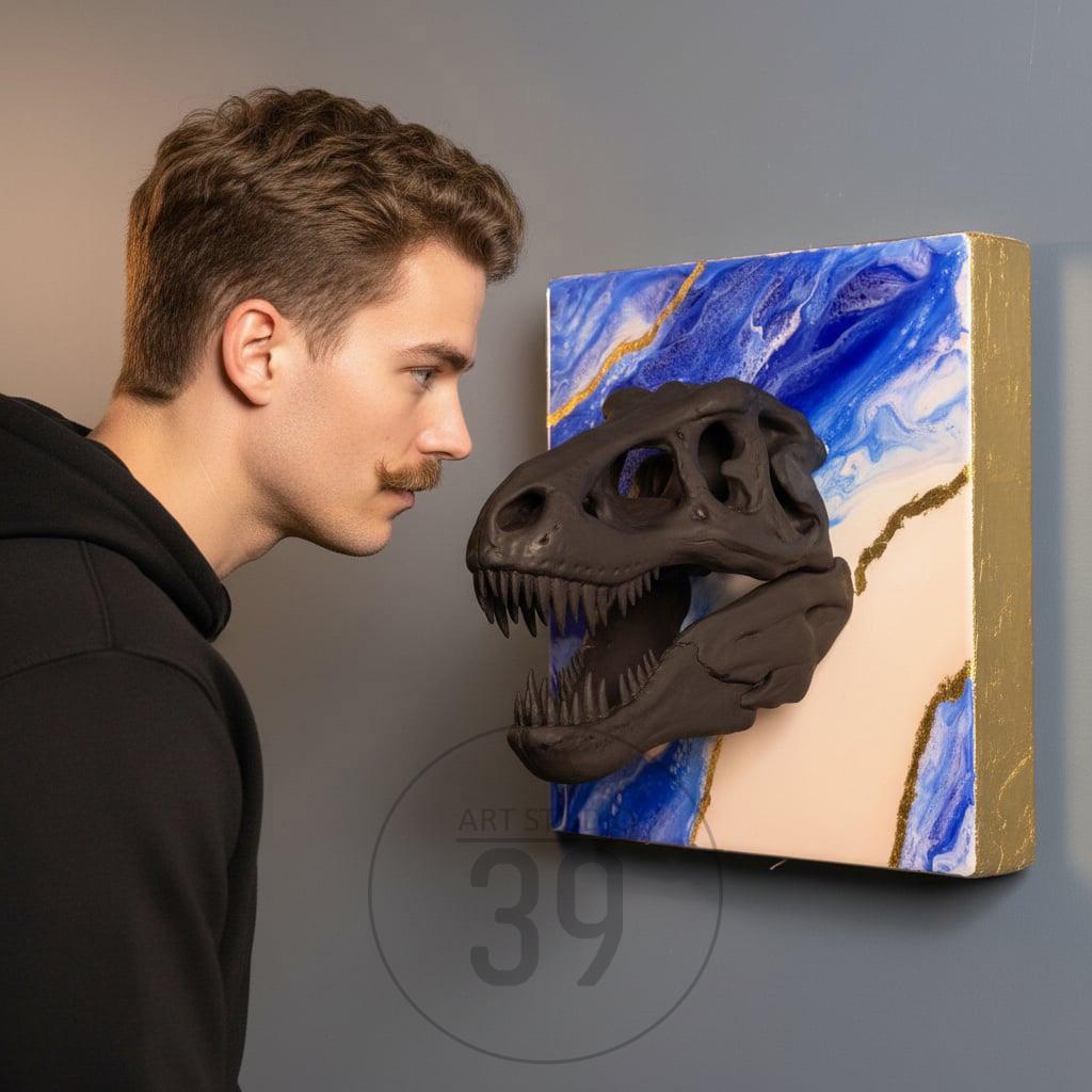 A black Tyrannosaurus Rex skull sculpture mounted on a square canvas. The canvas features a blue and white marbled design with gold accents. The artwork is displayed on a gray wall.
