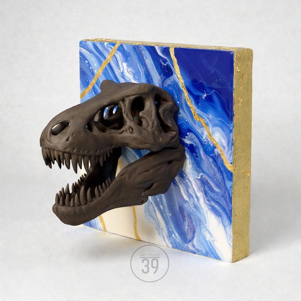 A dark brown dinosaur skull sculpture mounted on a square canvas. The canvas features a blue and white marbled design with gold accents. The sides of the canvas are painted gold. The sculpture is a unique piece of art.