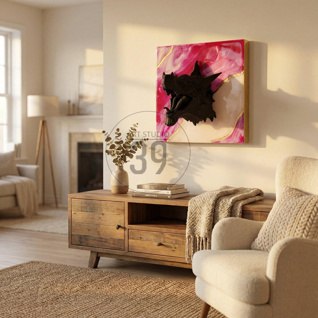 A black dragon head sculpture mounted on a square canvas with a pink and white abstract background and gold accents. The artwork is displayed in a living room setting, above a wooden cabinet.