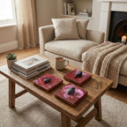 Three square coasters with a dark red and pink design, each topped with a black decorative element: a spider, a bird skull, and a heart. The coasters sit on a rustic wooden coffee table.