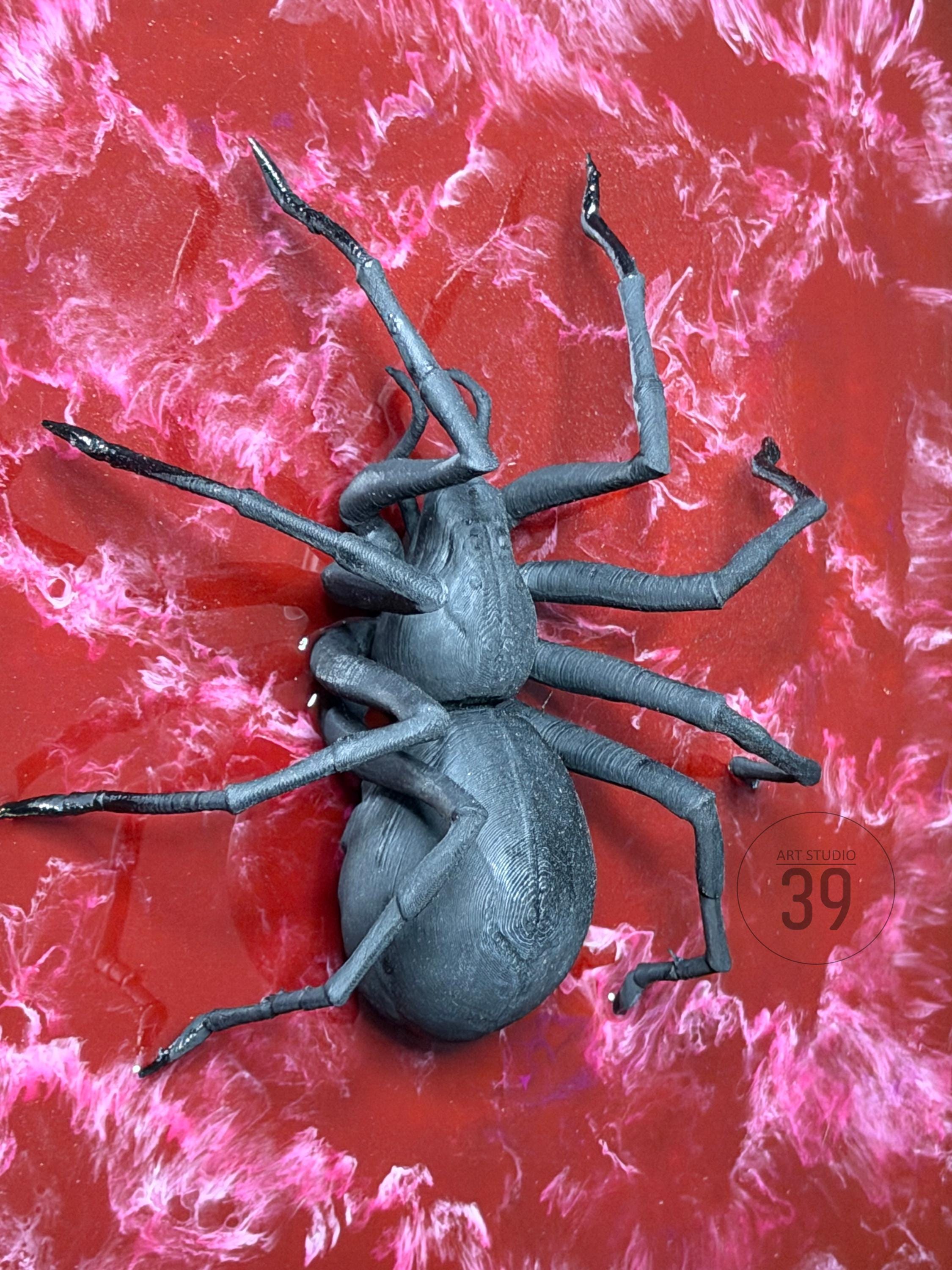 A dark gray, stylized insect sculpture with multiple legs and a segmented body. The sculpture is set against a vibrant red background with pink marbling. The text "ART STUDIO 39" is visible.