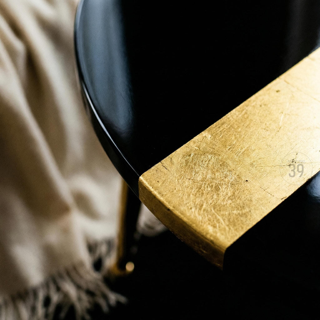 Close-up of a black, glossy table with a gold leaf accent on the edge. The table has a rounded shape and a dark finish. The gold leaf adds a touch of luxury and contrast to the design.