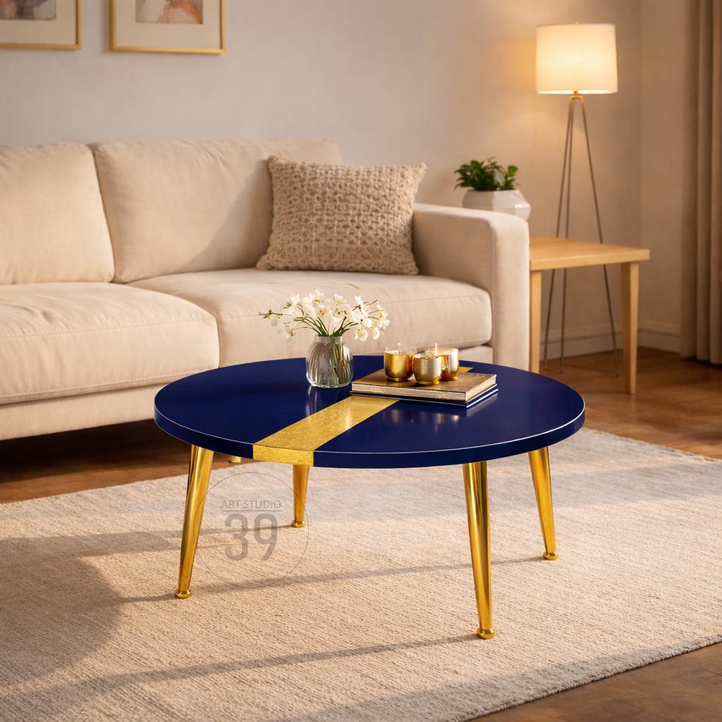 A round coffee table with a navy blue top and gold accents. The table has a gold stripe across the top and gold legs. The table is approximately 36 inches in diameter.