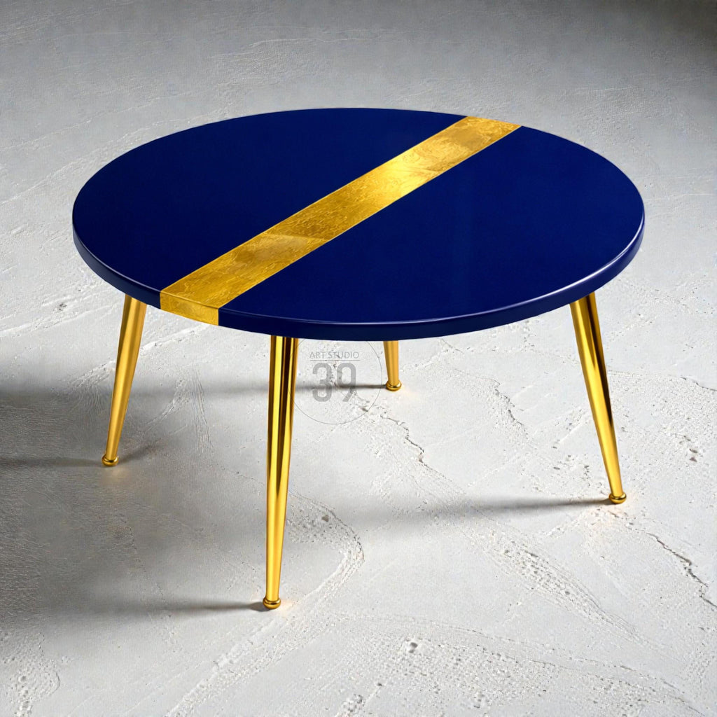 A round, navy blue coffee table with a gold stripe across the top. The table has gold-colored, angled legs. The table is a modern design and would be a great addition to any living room.