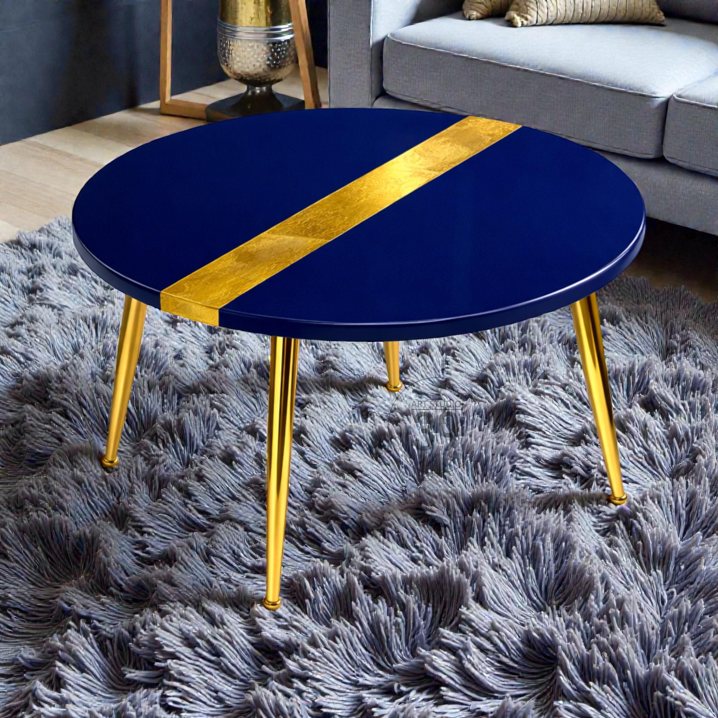 A round coffee table with a navy blue top and gold accents. The table has a gold stripe across the top and gold legs. The table is sitting on a gray shag rug.