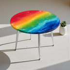A round side table with a rainbow-colored epoxy resin top. The table has a vibrant design with red, orange, yellow, green, and blue hues. It features silver metal legs and a small succulent in a white pot.