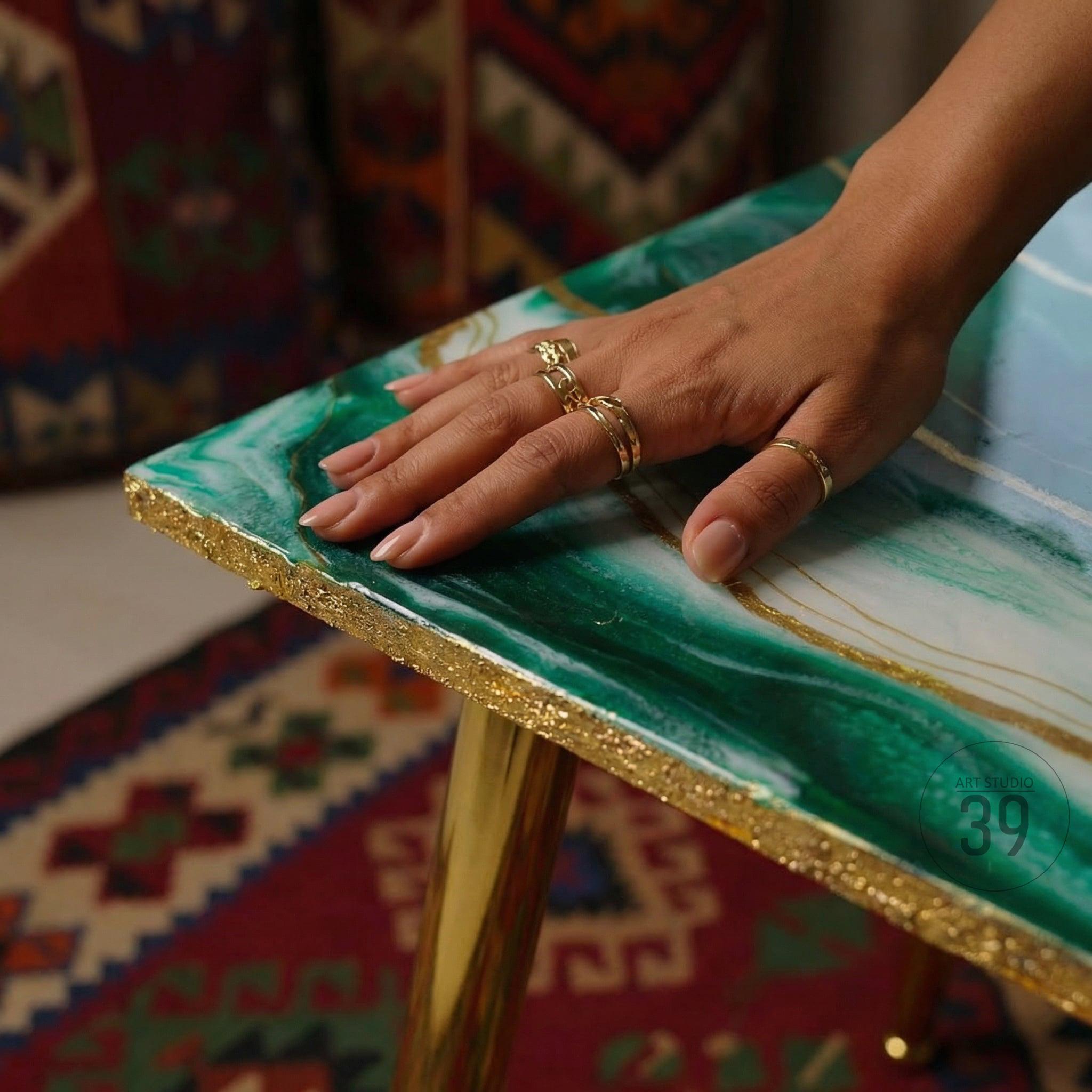 A rectangular table with a green and white marbled surface and gold trim. The table has gold legs and is accented with gold rings. The table's design is reminiscent of agate stone.