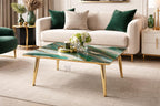 A modern living room scene featuring a square coffee table with a green and gold marble-effect top and gold legs. The table is in front of a cream-colored sofa with green and beige pillows. Decorative vases and flowers are on the table.