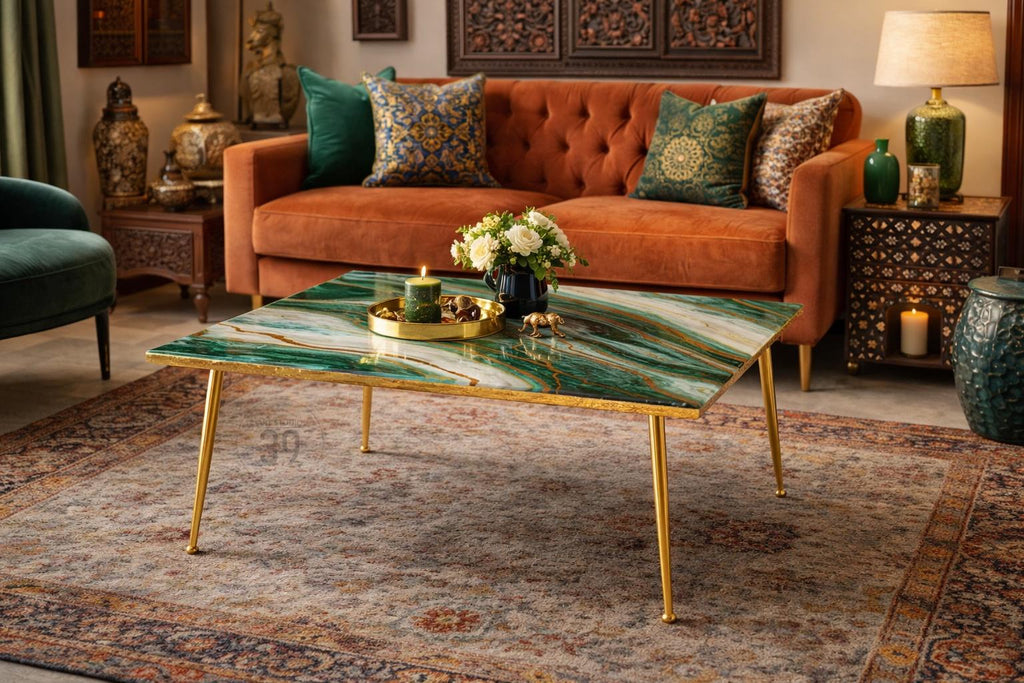 A living room scene featuring a green and gold coffee table with gold legs. The table has a marble-like pattern. An orange velvet sofa with decorative pillows is in the background. A rug and other decorative items complete the scene.