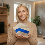 A person holding a stack of wooden coasters. Each coaster features a natural wood grain pattern with a vibrant blue resin stripe. The coasters are square and appear to be handmade. The image has a warm, inviting aesthetic.
