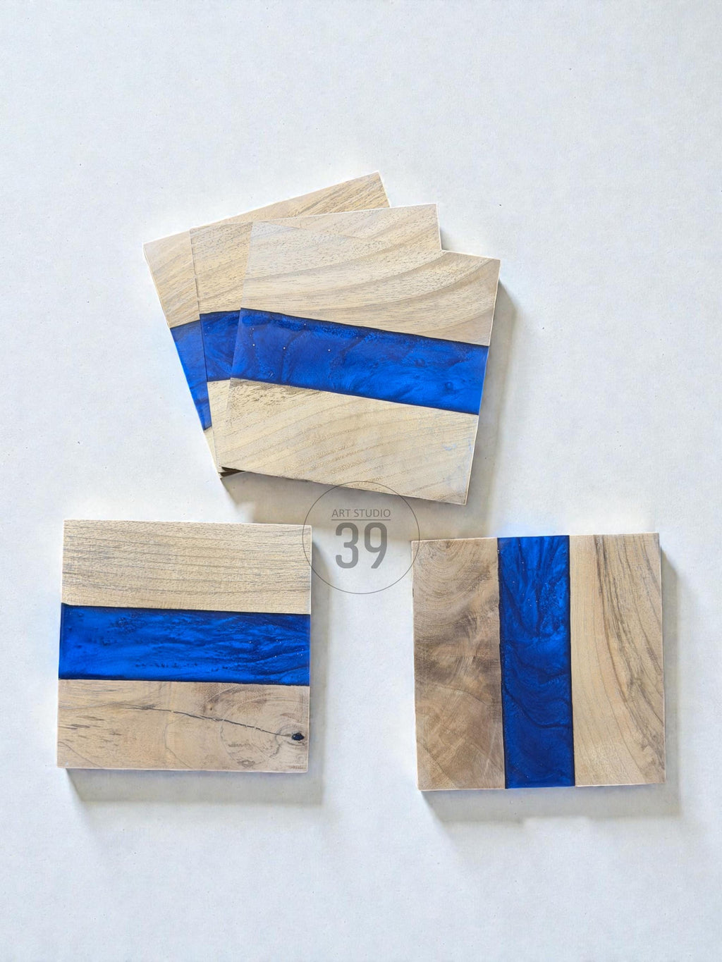 Wooden coasters with a blue resin stripe. The coasters are square-shaped and made of light-colored wood. The blue resin adds a pop of color and a modern touch. The coasters are arranged on a white surface.