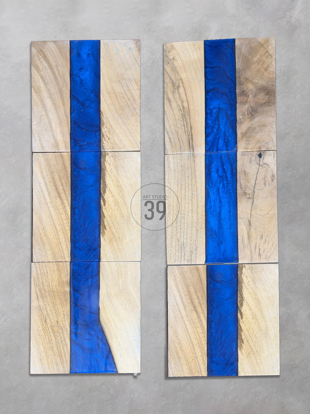 Set of six wooden coasters with a blue resin river design. The coasters are rectangular with a natural wood grain and a vibrant blue stripe running down the center. The text "ART STUDIO 39" is visible.