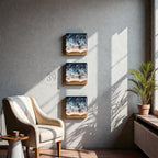 Three square wall art pieces depicting ocean waves with blue, white, and tan hues. The artwork is mounted on a gray wall, with a beige armchair and a small side table in the foreground. A potted plant sits near a window.