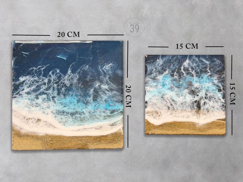 Two square resin art pieces depicting an ocean scene with waves and a golden beach. The larger piece is 20 cm (7.9 in) square, and the smaller is 15 cm (5.9 in) square. The artwork features shades of blue, white, and gold.