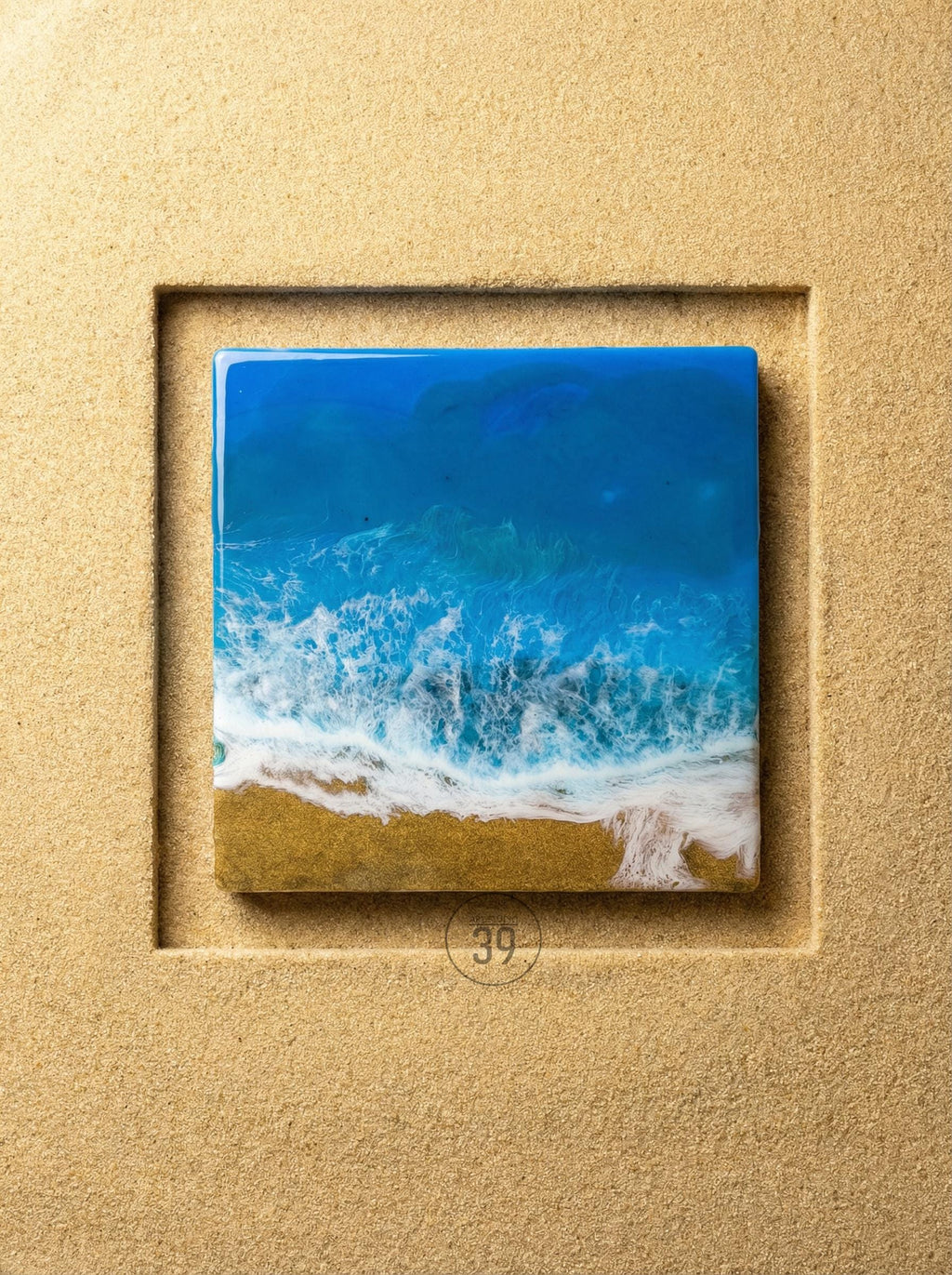 Square resin art piece depicting an ocean scene with blue and white waves crashing onto a golden sand beach. The artwork is set within a textured, light brown frame. The number "39" is in a circle at the bottom.