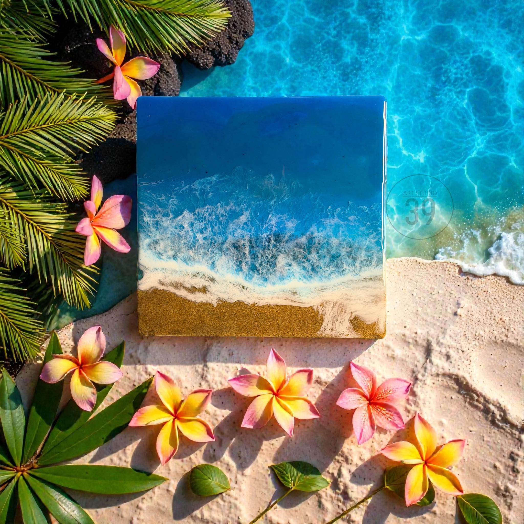 Square resin art piece depicting a beach scene with blue ocean waves, golden sand, and white foam. The artwork is surrounded by pink and yellow plumeria flowers, green leaves, and palm fronds, creating a tropical theme.