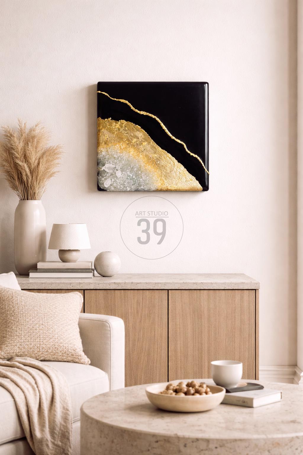 Square black and gold abstract art piece with a gold vein design. The artwork is mounted on a white wall above a wooden cabinet. The text "ART STUDIO 39" is in a circle below the artwork.